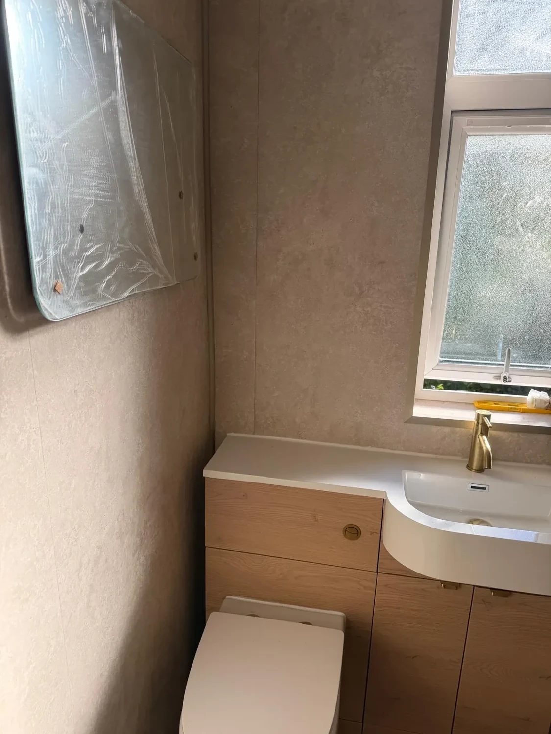 Oak-effect vanity and toilet unit beneath a frosted window
