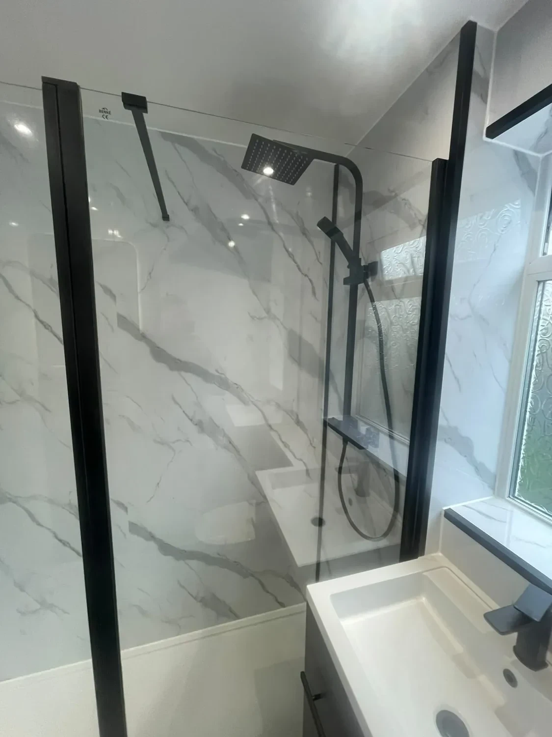 Black rainfall shower and glass screen against pale marble-effect panels